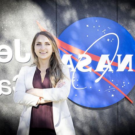 A woman stands in front of a NASA sign with her arms folded.